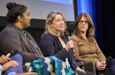 three women faculty members on stage, one holding mic and speaking