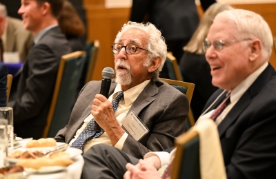Man with white hair and goatee seated with microphone