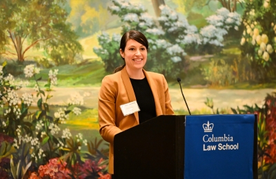 Dark-haired woman in brown jacket smiling at podium