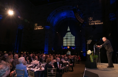 Man at podium on stage addressing Winter Luncheon guests seated at tables