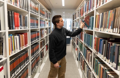 A student reaches to take a book off a bookshelf in the library.