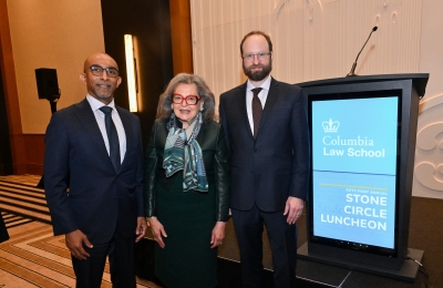 Dean Daniel Abebe, Susan Lindenauer, and Professor Jeremy Kessler smile standing next to a blue podium that says Columbia Law School Stone Circle Luncheon on the front.