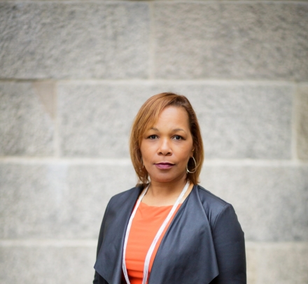 Woman in orange dress, pearls and gray jacket