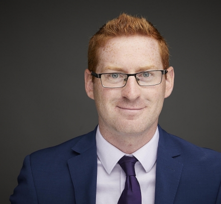 Red-headed man wearing glasses, a blue jacket, and a tie