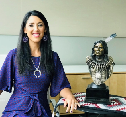 Woman in purple dress next to bust of Native American leader