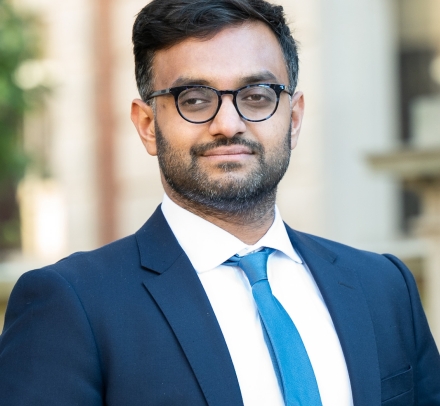 Professor Ashraf Ahmed smiling. He wears glasses with a blue suit and necktie.