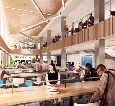 Students sit at long tables next to a bank of windows and beneath a mezzanine.