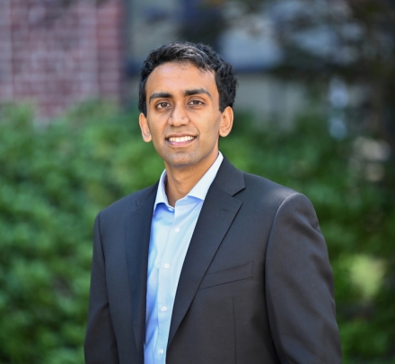 Neel Guha in blazer and light blue shirt standing outside with green bushes in background
