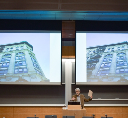 Professor Vincent Blasi gestures in front of a screen featuring a multistory building.