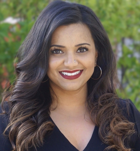 Devi Patel, smiling with an ivy-covered wall behind her