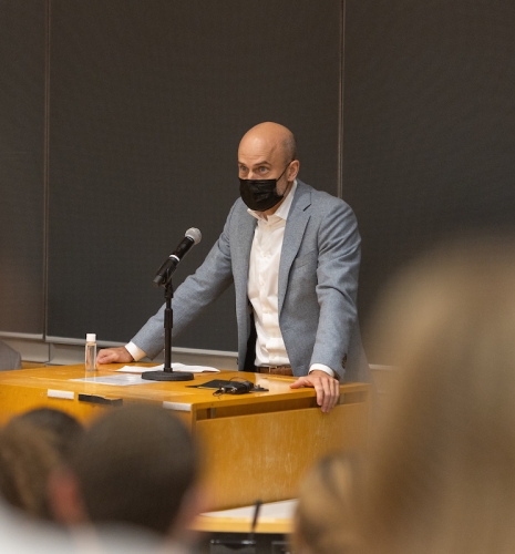 Man in blazer at podium in front of blackboard