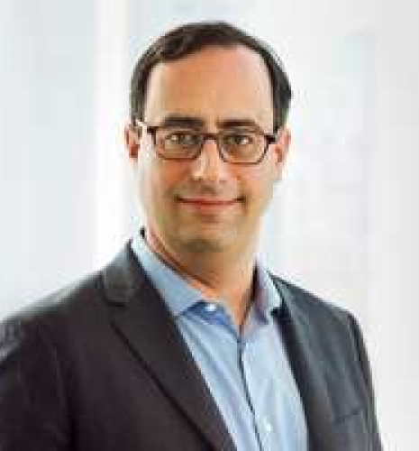 Man with short brown hair and glasses wearing a blue collared shirt and gray blazer