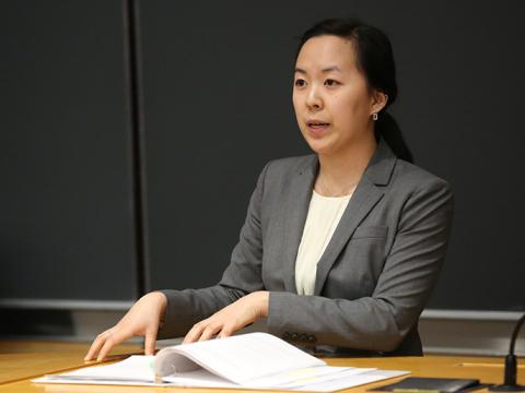 A student in a grey blazer speaks at a podium.