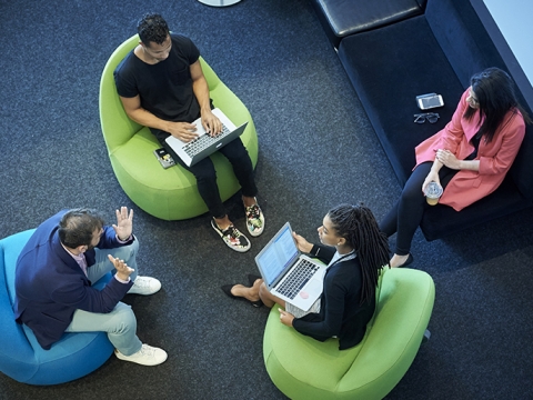 Students sit a circle of brightly colored chairs.
