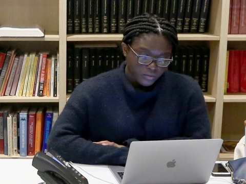 A student working on a laptop in front of a bookshelf