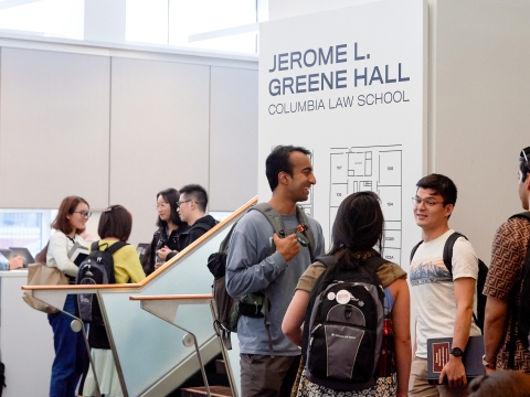 Students stand in groups in the Jerome Greene Hall lobby and talk.