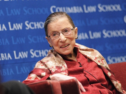 Ruth Bader Ginsburg smiles in front of a blue Columbia Law School backdrop