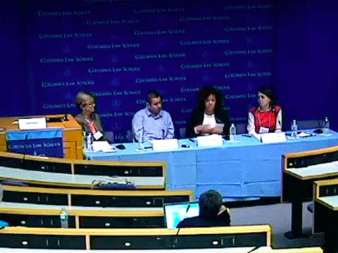 Four people sit behind a table with microphones and water bottles.