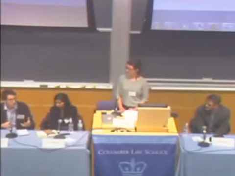 A woman stands at a podium in a lecture hall.