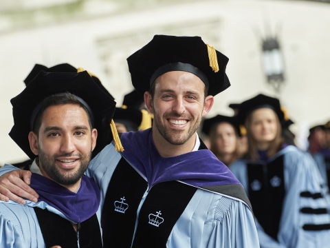 Two students smile in their graduation regalia