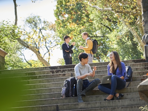 Two students talk while sitting on park steps, two students stand behind them