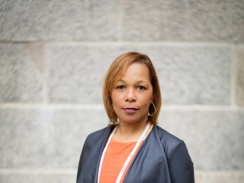 Woman in orange dress, pearls and gray jacket