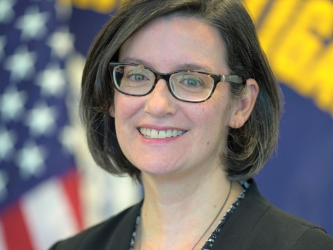 Woman with dark bobbed hair and glasses in front of American flag