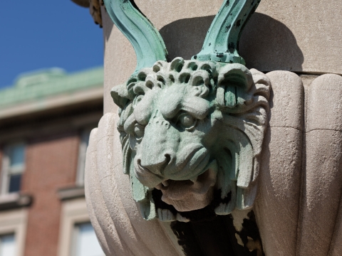 A decorative copper lion's head on a cement urn on campus