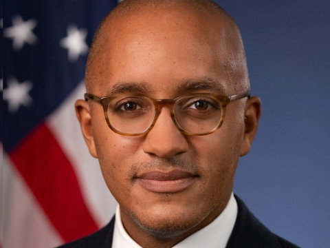Headshot of a man wearing glasses, white shirt, blue tie, and black blazer