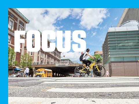 The word FOCUS superimposed over an image of a person riding a bicycle outside the Law School