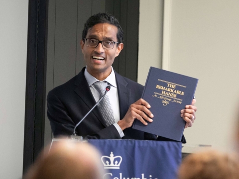 Man in suit and tie holds book at podium