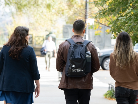 Three students, one of whom wears a Columbia Law backpack, walk on a sidewalk.
