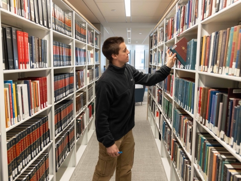 A student reaches to take a book off a bookshelf in the library.