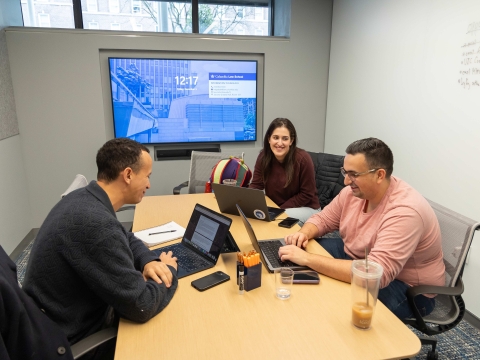 Students work on laptops at table in a group study room in the library.