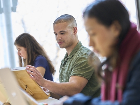 Three people sitting with the one in the middle reading a book