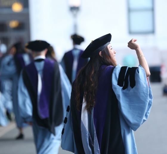 A female graduate waving and wearing regalia at Law School graduation.