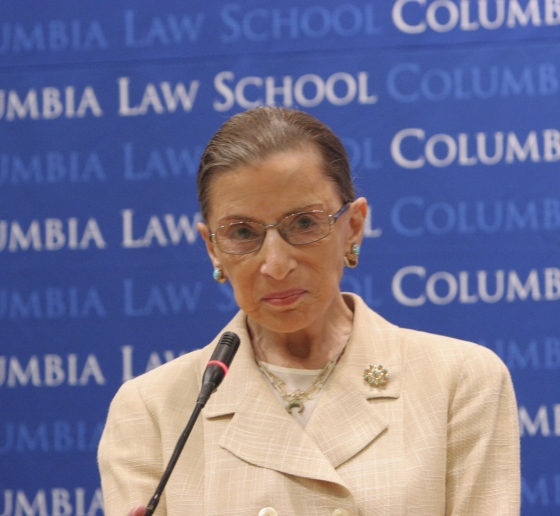Ruth Bader Ginsburg standing at a podium in front of a Columbia Law School step and repeat