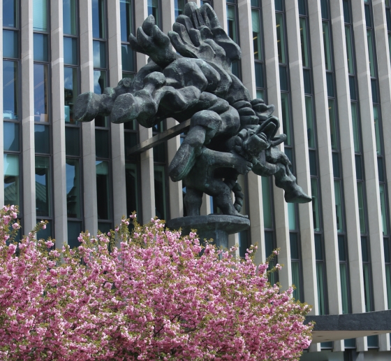 Tree with pink flowers and massive sculpture in front of modern building
