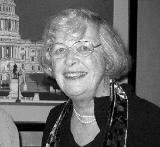 Woman with glasses and gray hair, wearing black jacket and pearls