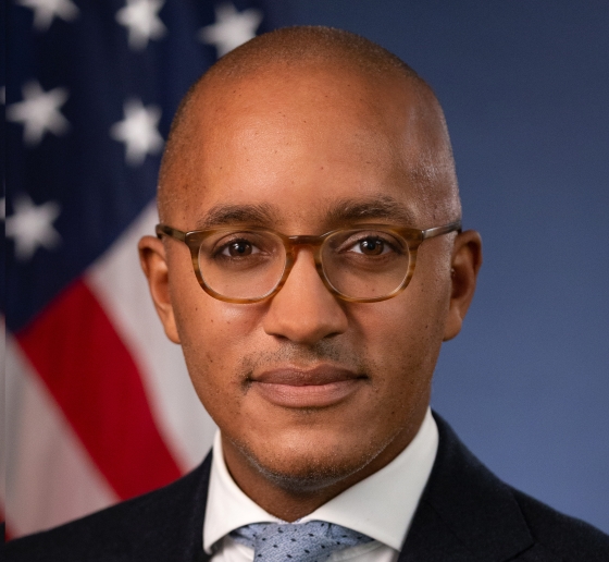 Headshot of a man wearing glasses, white shirt, blue tie, and black blazer