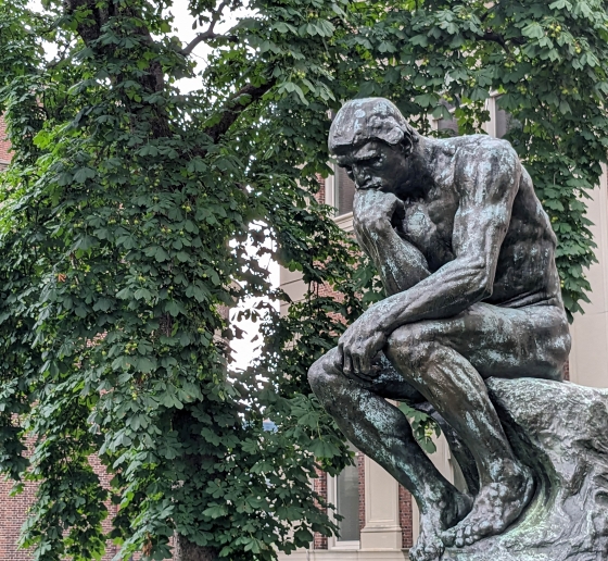 The statue Thinker in front of a green tree in summer