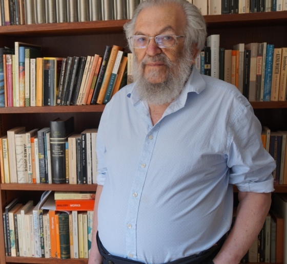 Beareded man in front of wall of bookshelves