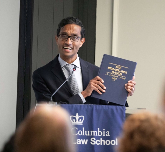 Man in suit and tie holds book at podium