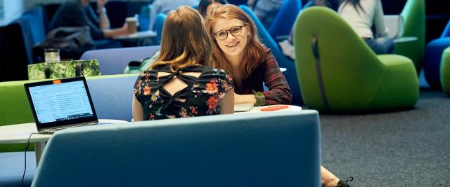 Two students speak to each other in the lobby of Jerome Greene Hall.