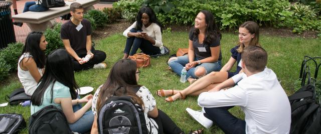 A group of students sit in a circle in the grass.