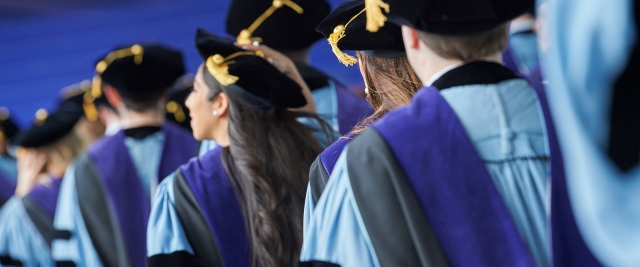 Students at graduation wearing caps and gowns, seen from behind