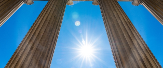 Four columns of a building behind which is the sun