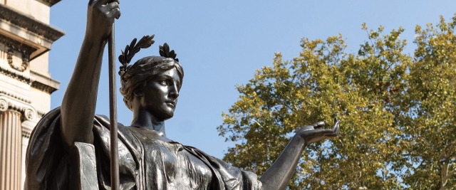 Alma Mater statue seen from west with autumn leaves behind it