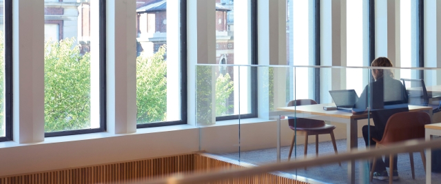 A person studies with a laptop at a table by a bank of windows in the library.