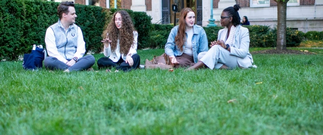 Four law students sit in the grass talking to each other.